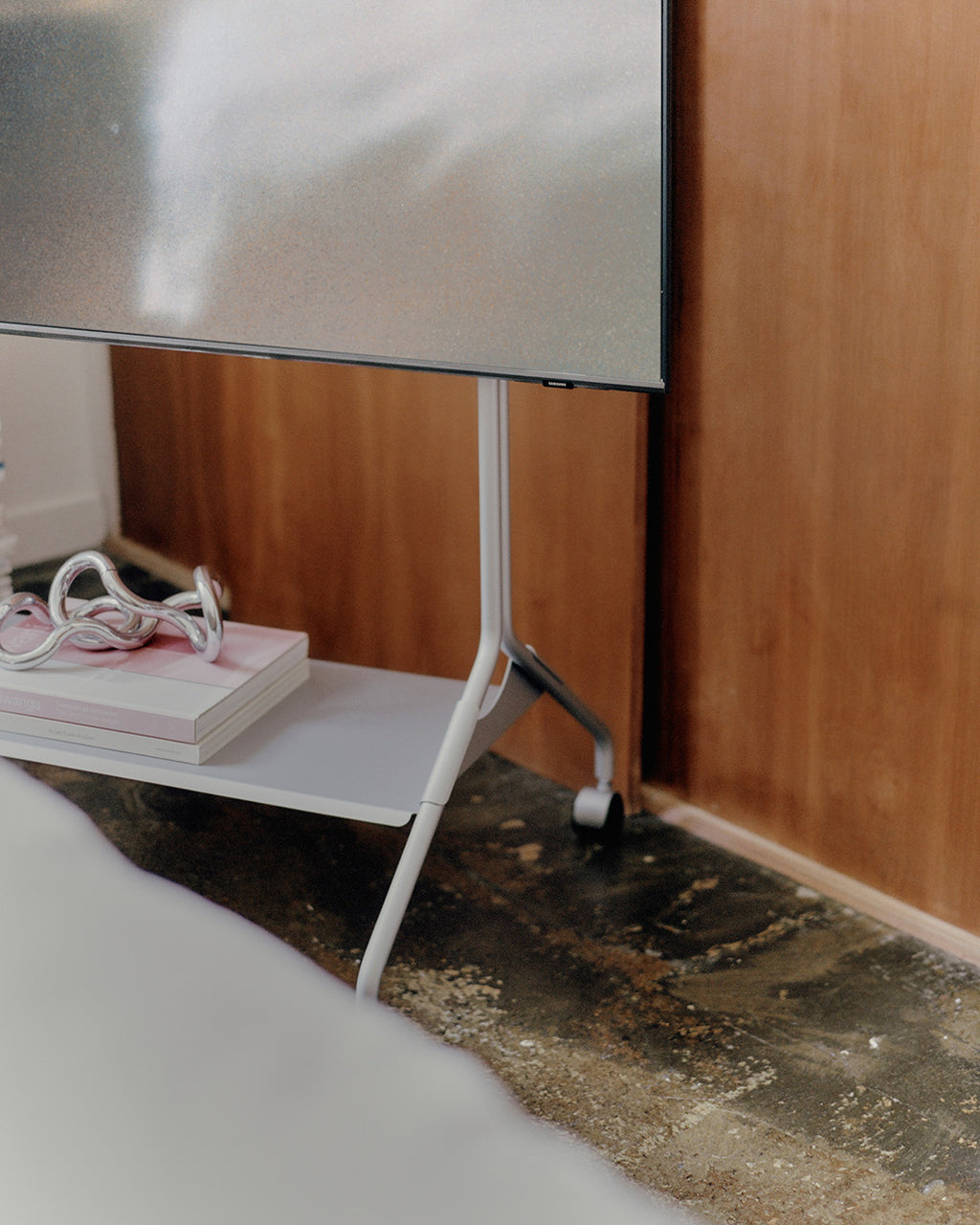 Detalle del Moon in Cloudy Silver con ruedas y TV montado, junto a pared de madera y estante con libros