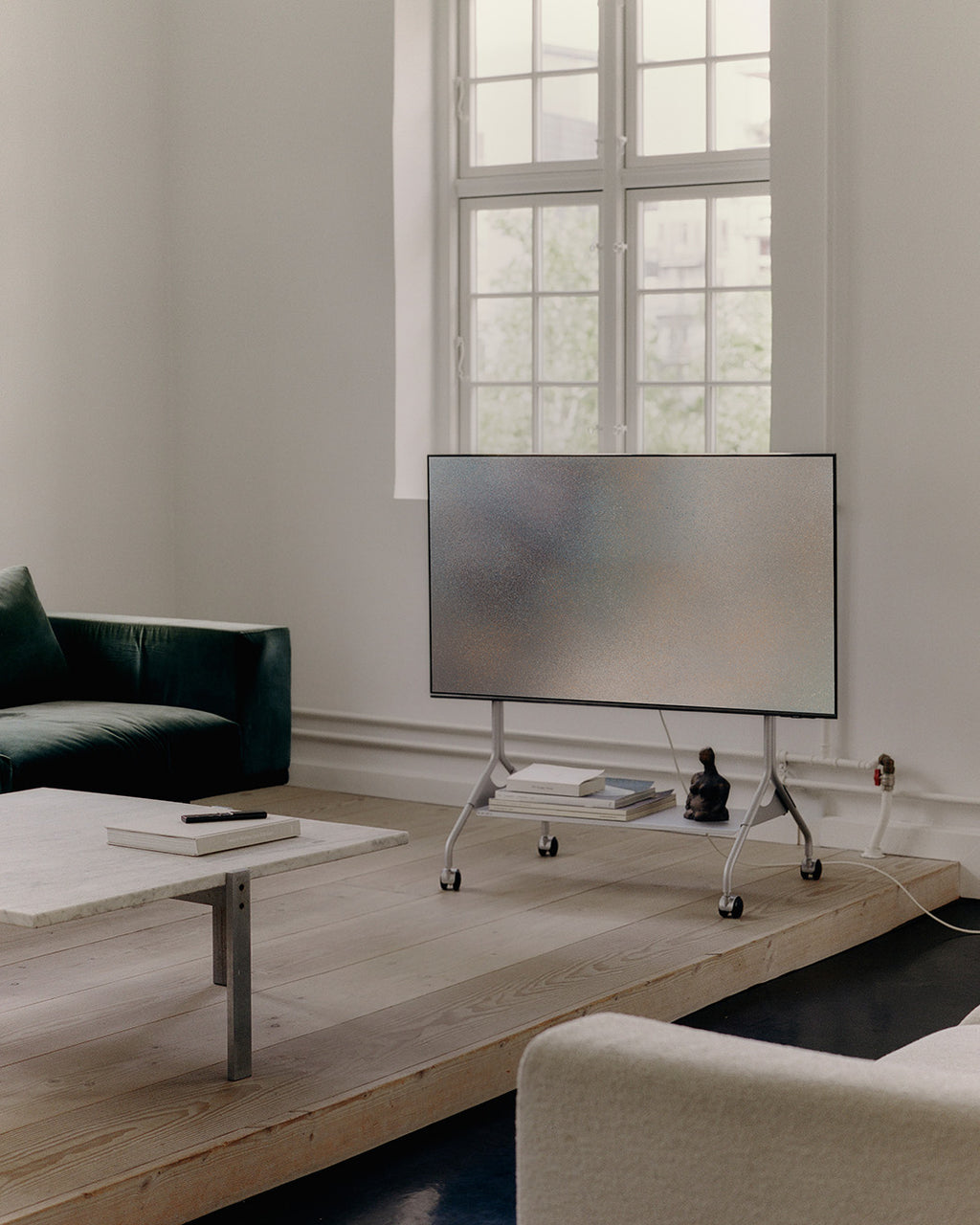 Soporte Moon in Cloudy Silver con ruedas y TV en salón minimalista, junto a sofá verde y mesa de mármol