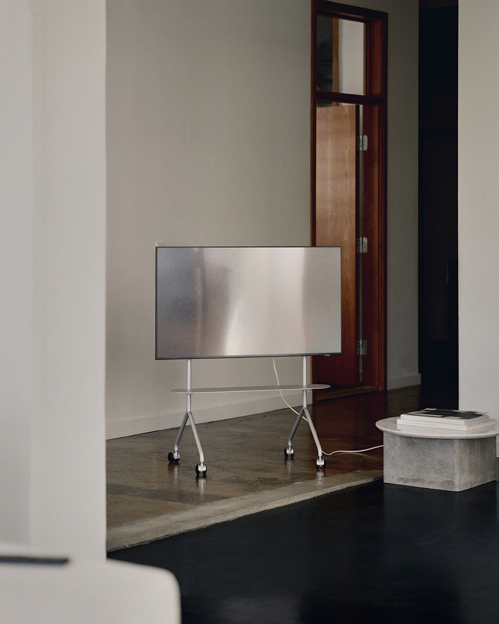 Soporte con ruedas Moon Light in Cloudy Silver con TV en sala minimalista junto a puerta de madera y mesa de piedra