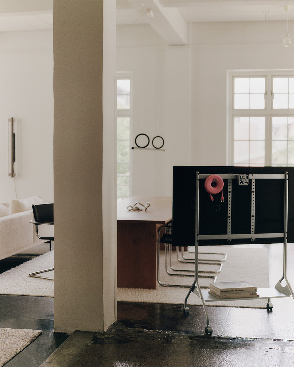 Soporte Moon Tall en Cloudy Silver con ruedas y TV en loft minimalista, visto desde atrás junto a libros apilados